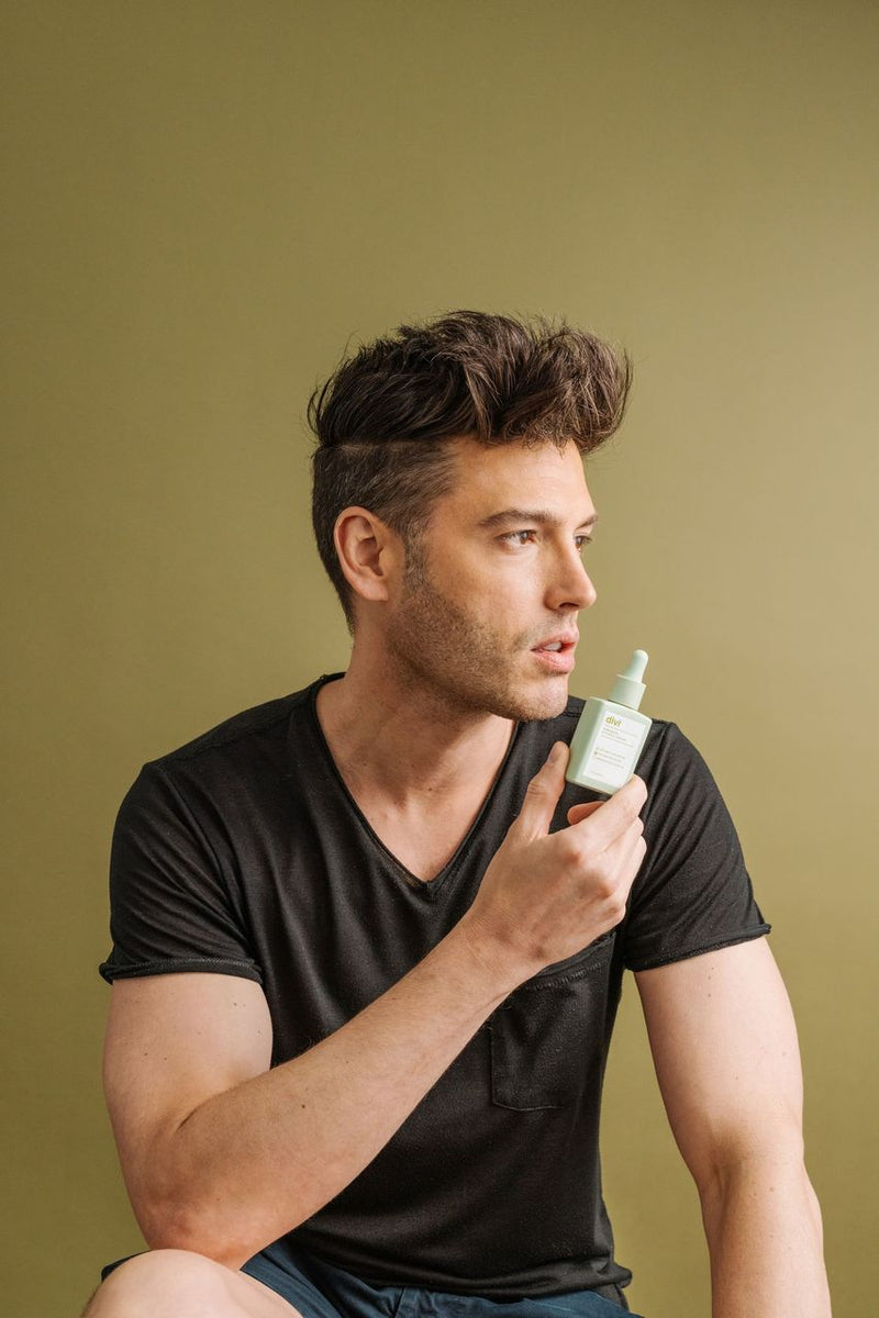 A young man holding a bottle of Divi's Scalp Serum